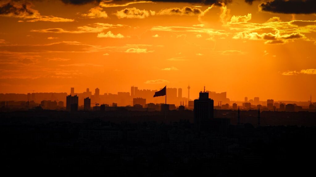 Dramatic orange sunset over Istanbul's skyline, featuring iconic landmarks and a Turkish flag.